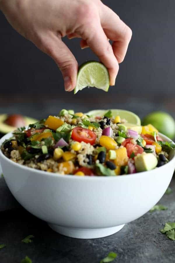 Tex-Mex Quinoa Salad in a white bowl with a lime being squeezed over it