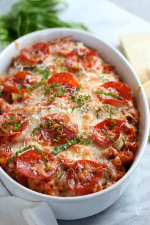 Close up of casserole dish with quinoa topped with melted cheese, pepperoni and fresh basil. 