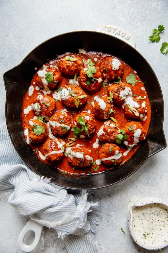 Buffalo Chicken Meatballs in a cast iron skillet drizzled with ranch and topped with green onion and cilantro.