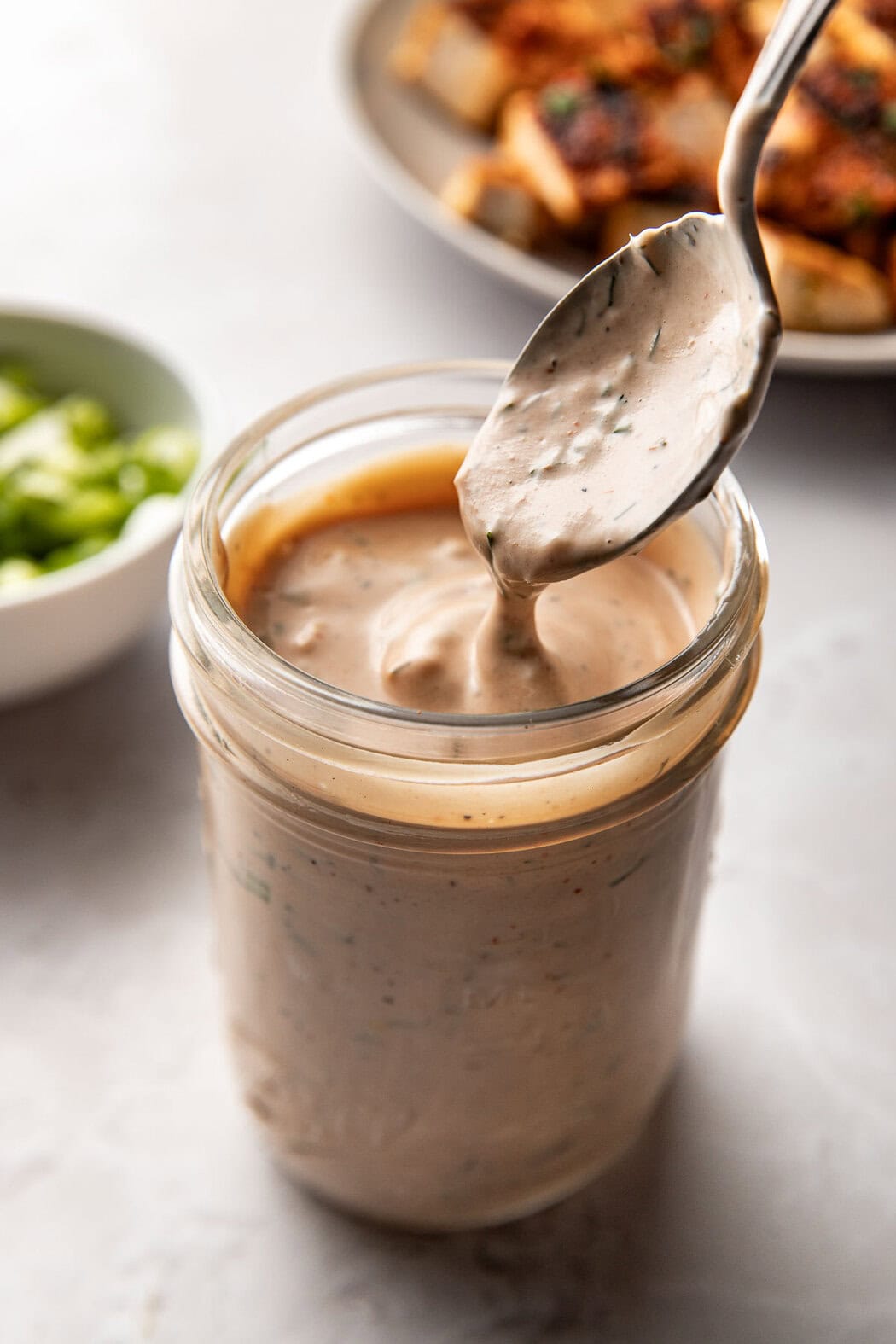 Close up view of a mason jar filled with homemade BBQ ranch sauce with a spoon coming out to show the thickness and texture of the sauce. 