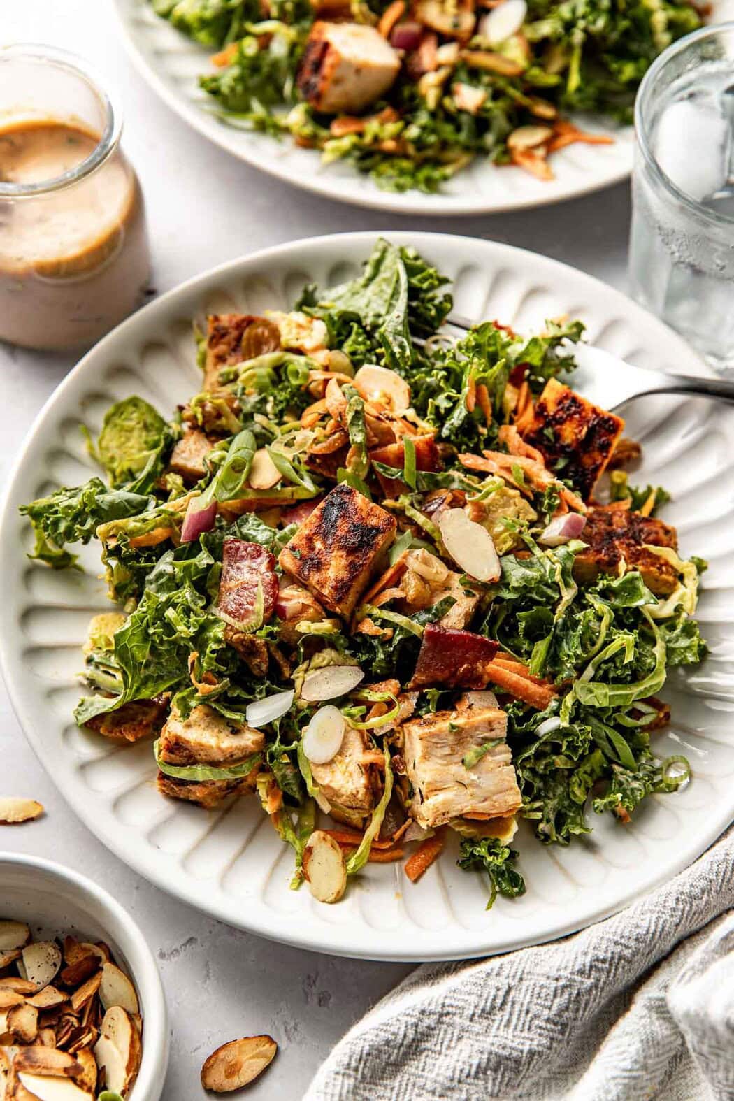Close up view of a white plate of colorful greens and vegetables topped with Blackened Chicken pieces and green onions. 