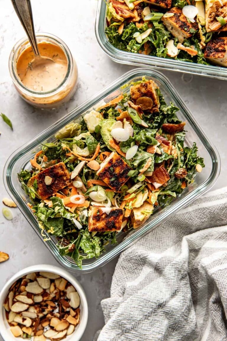 Overhead view of two glass meal prep containers filled with chopped BBQ ranch chicken salad topped with green onions and sliced almonds.