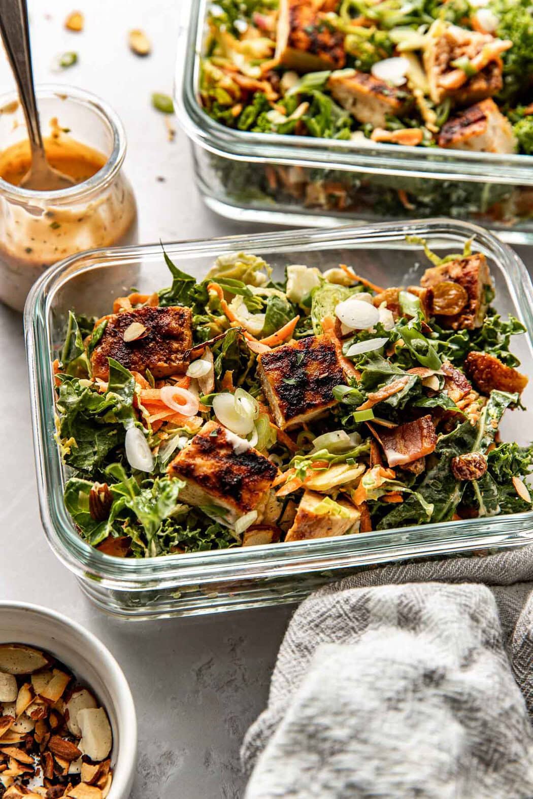 Close up view of Chopped BBQ Ranch Chicken Salad in two glass meal prep containers topped with green onions and toasted sliced almonds. 