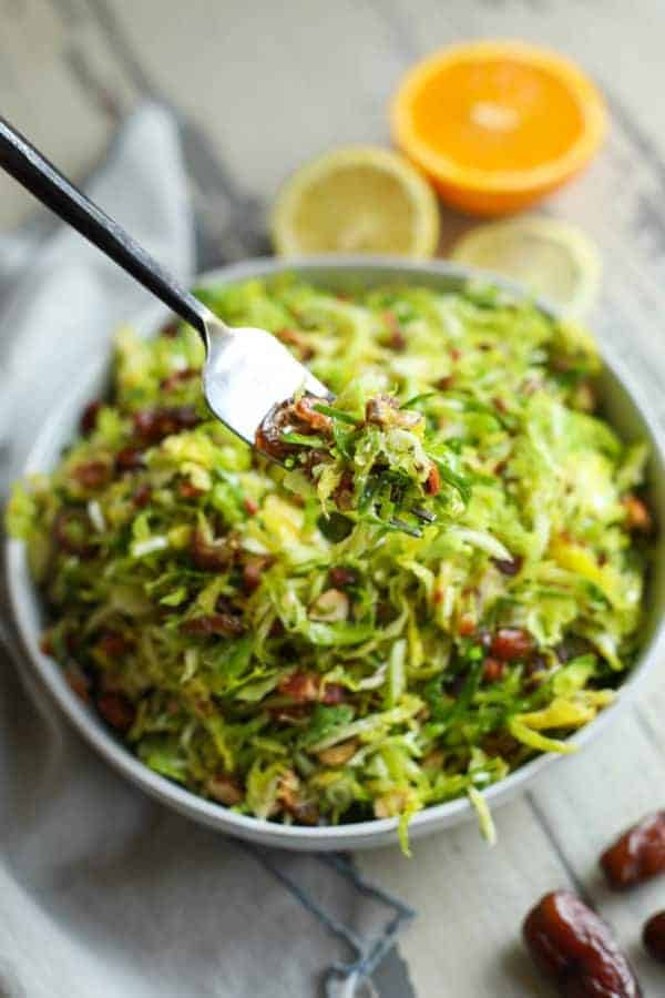 Shredded Brussels sprouts salad in a bowl with a fork bringing a bite up to the camera. 