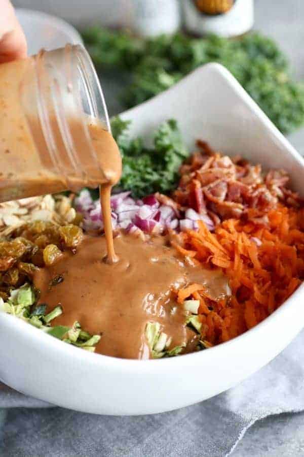 BBQ Ranch Chopped Salad with Brussels Sprouts & Kale ingredients in a white bowl with dressing being poured over it