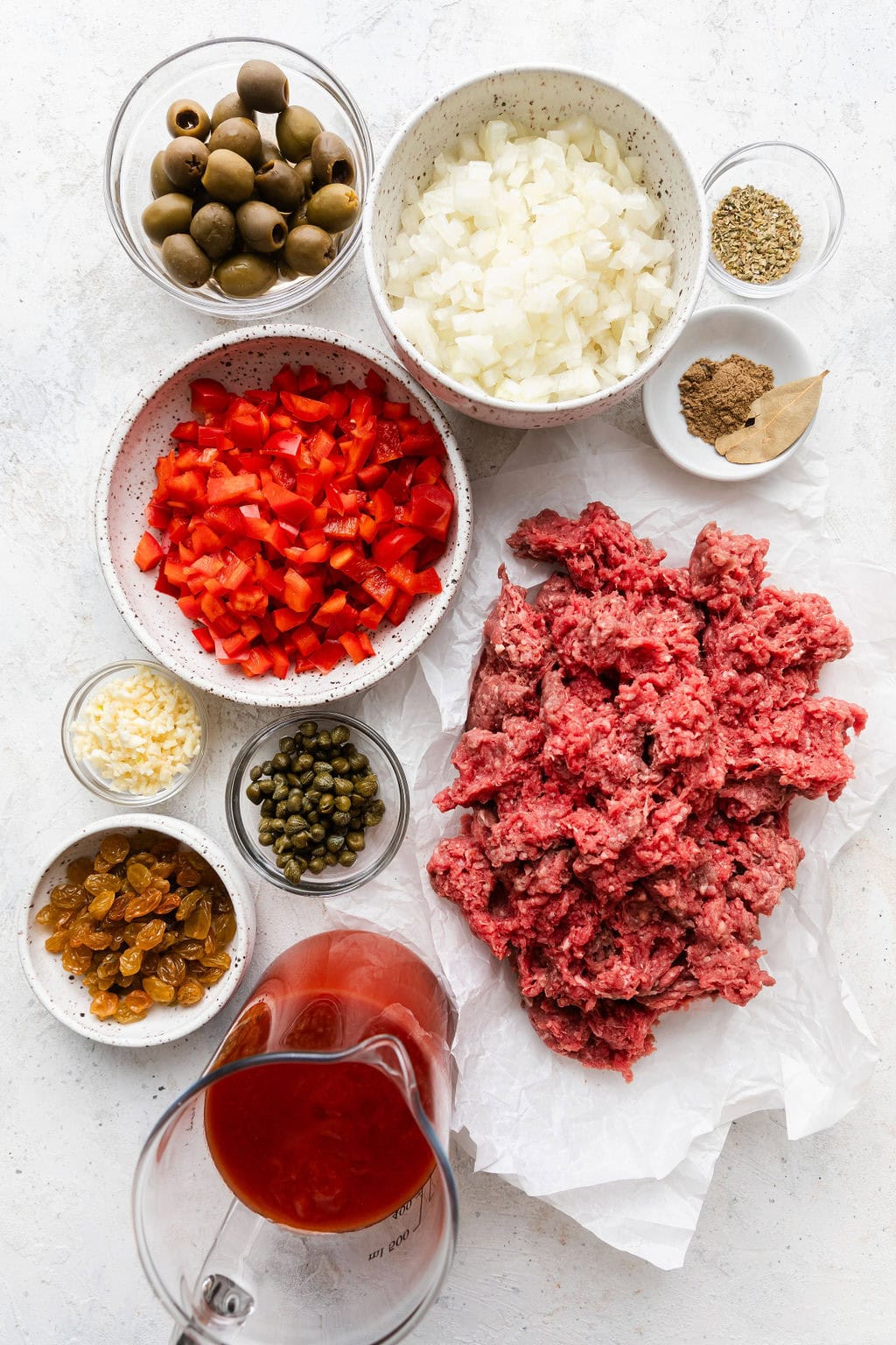 Overhead view of a variety of ingredients for Stovetop Picadillo in different sized bowls. 