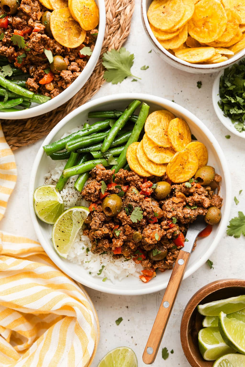 Overhead view of a plate of Stovetop Picadillo on top of rice and served with plantain chips and green beans. 