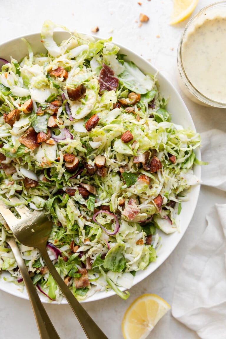 Overhead view of a serving bowl filled with sweet and smoky shredded brussels sprouts slaw topped with smoked almonds and salty bacon.