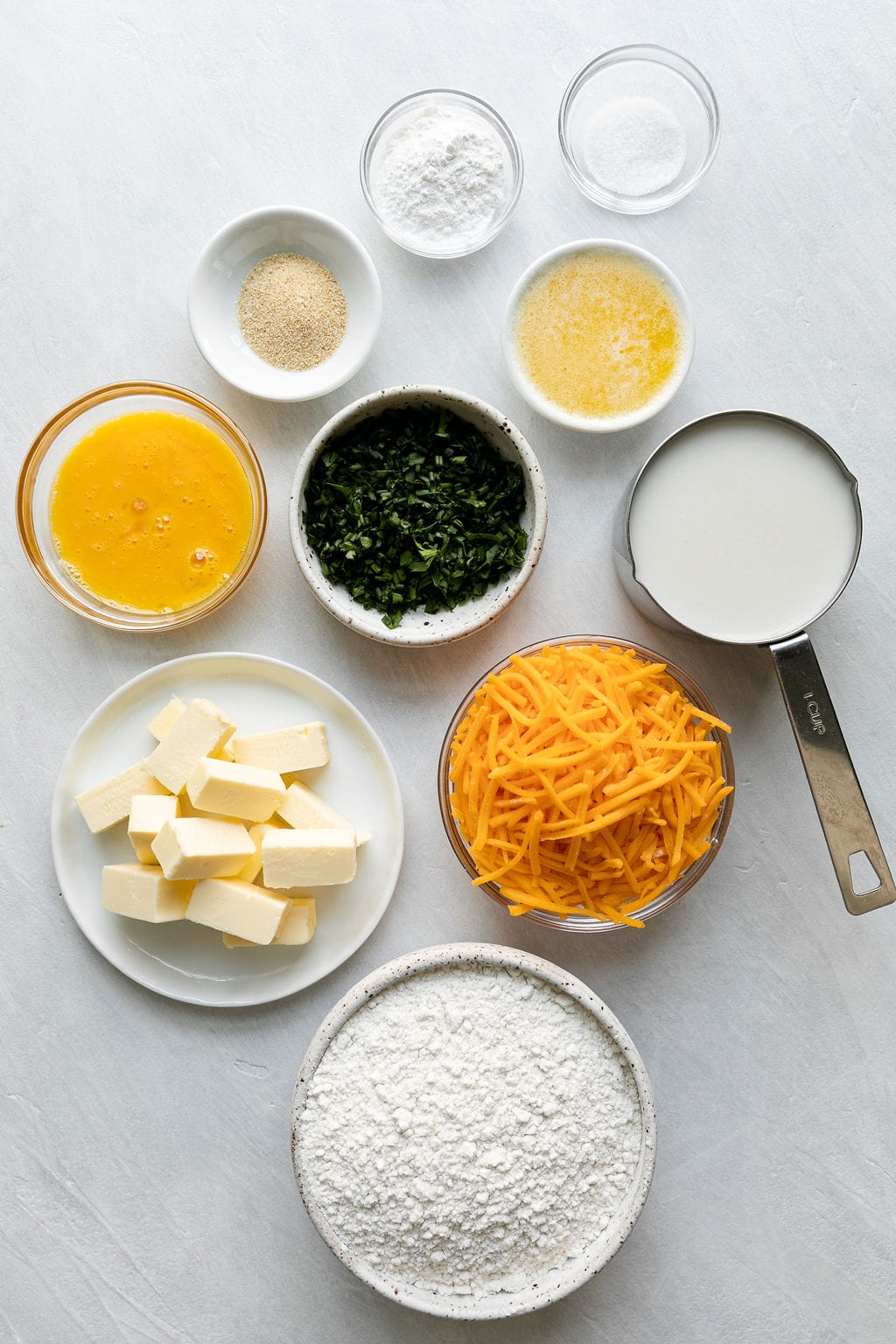 All ingredients for garlic cheddar gluten free biscuits arranged together in small bowls and measuring cups.