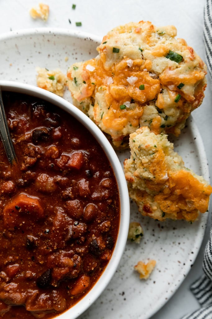 A gluten free cheddar biscuit on the side of a bowl of hearty chili.