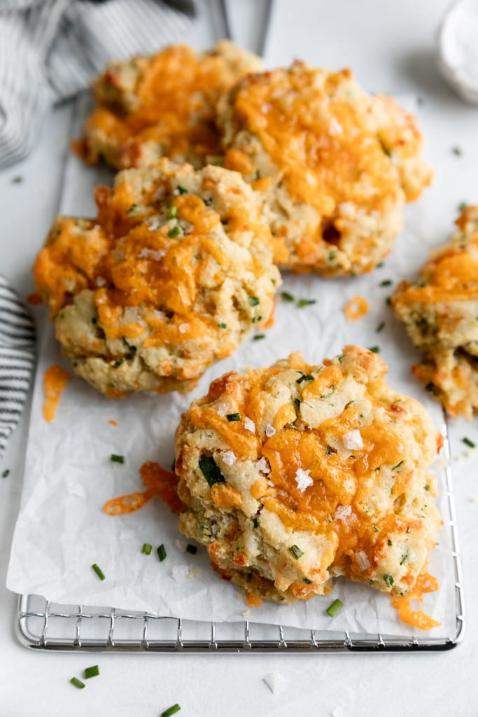 Garlic Cheddar Gluten-Free Biscuits on parchment-covered cooling rack topped with melted cheddar cheese shreds and flakey sea salt.