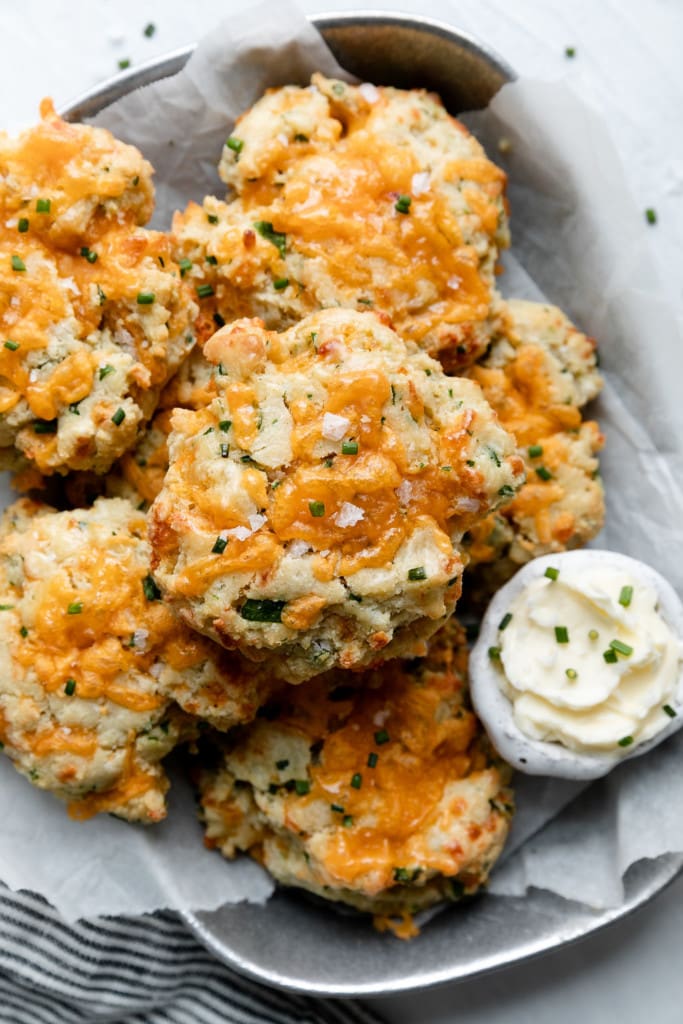A pile of garlic cheddar gluten free biscuits topped with melted cheddar cheese, chives, and flakey sea salt.