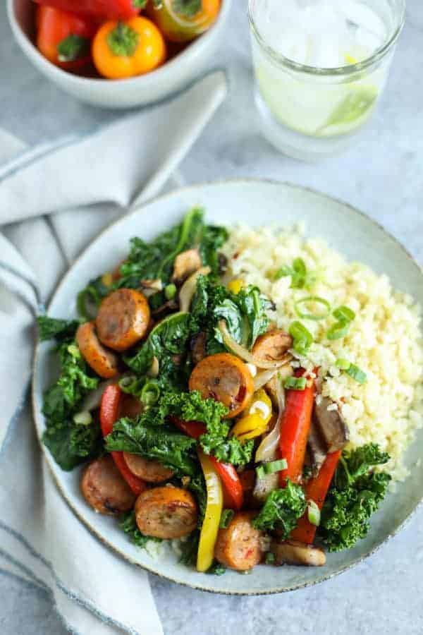 Overhead shot of Grilled Chicken Sausage and Veggies over Cauliflower Rice on table with a napkin and glass of water. 