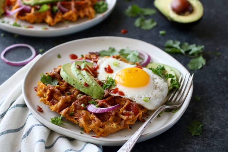 Savory sweet potato bacon waffles on plate topped with fried egg and avocado slices.