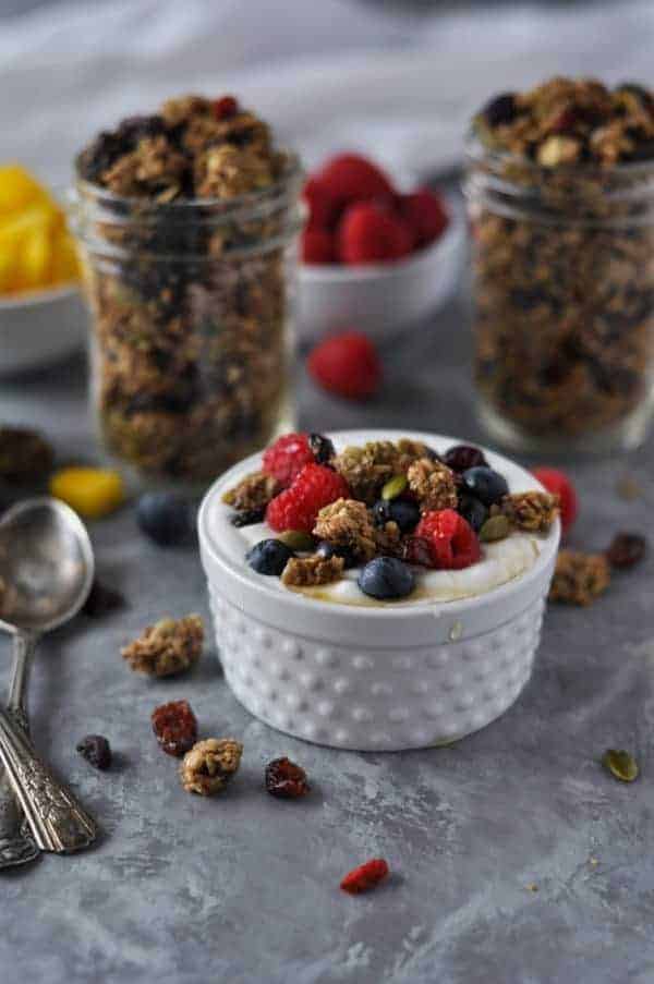 Crunchy Nut-free Paleo Granola served with yogurt, berries and a little honey in a small white bowl.