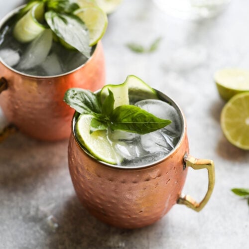 Two copped mugs filled with cucumber basil moscow mules.