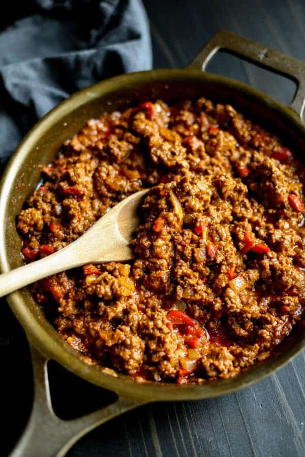 Ground beef browning in a skillet with a wooden spoon stirring the meat