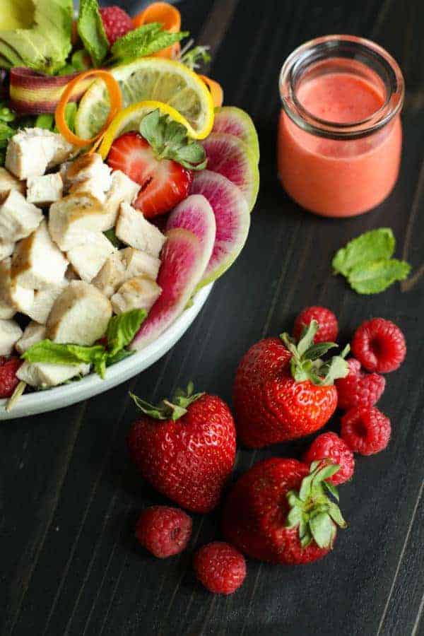 Berry Protein Salad Bowl ingredients in a white bowl with a focus on strawberries on the tabletop