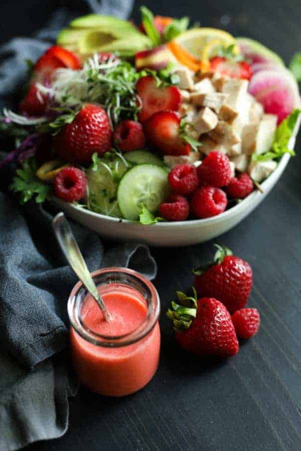 Berry Protein Salad Bowl in a white bowl with a side of vinaigrette and strawberries