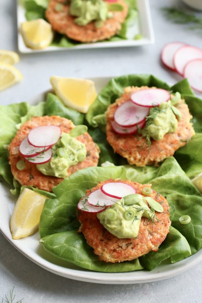 Salmon burgers on lettuce leaves topped with avocado sauce and sliced radishes