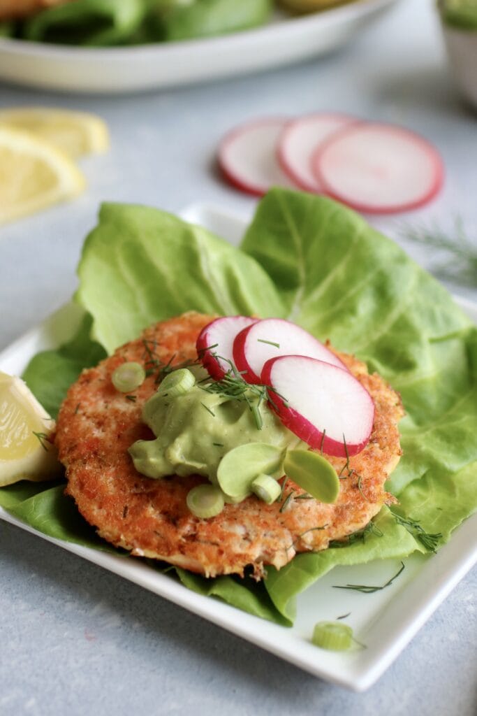 Close up side view salmon burger in lettuce topped with avocado sauce and sliced radish