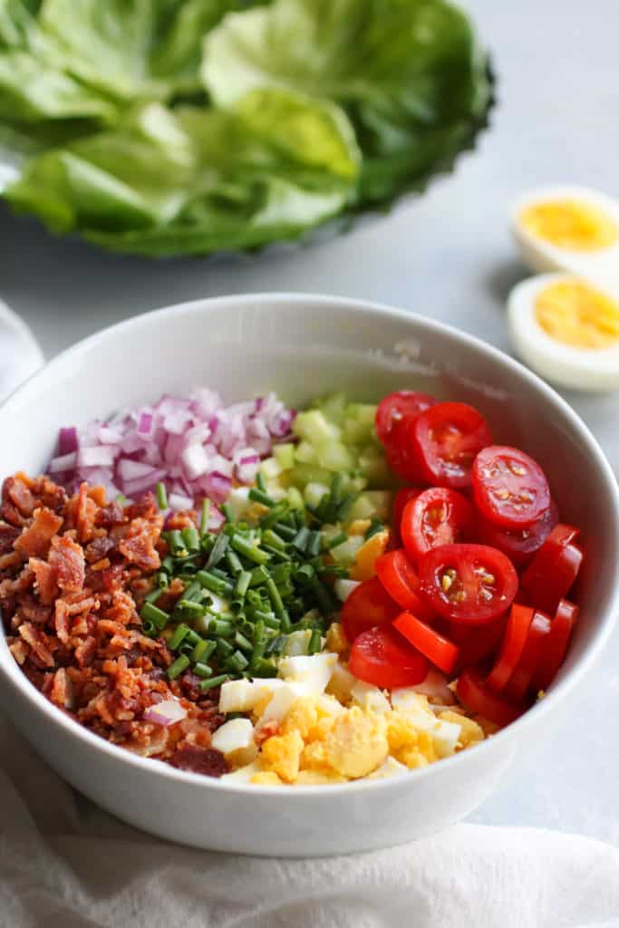 White bowl filled with all ingredients for BLT Egg Salad Wraps
