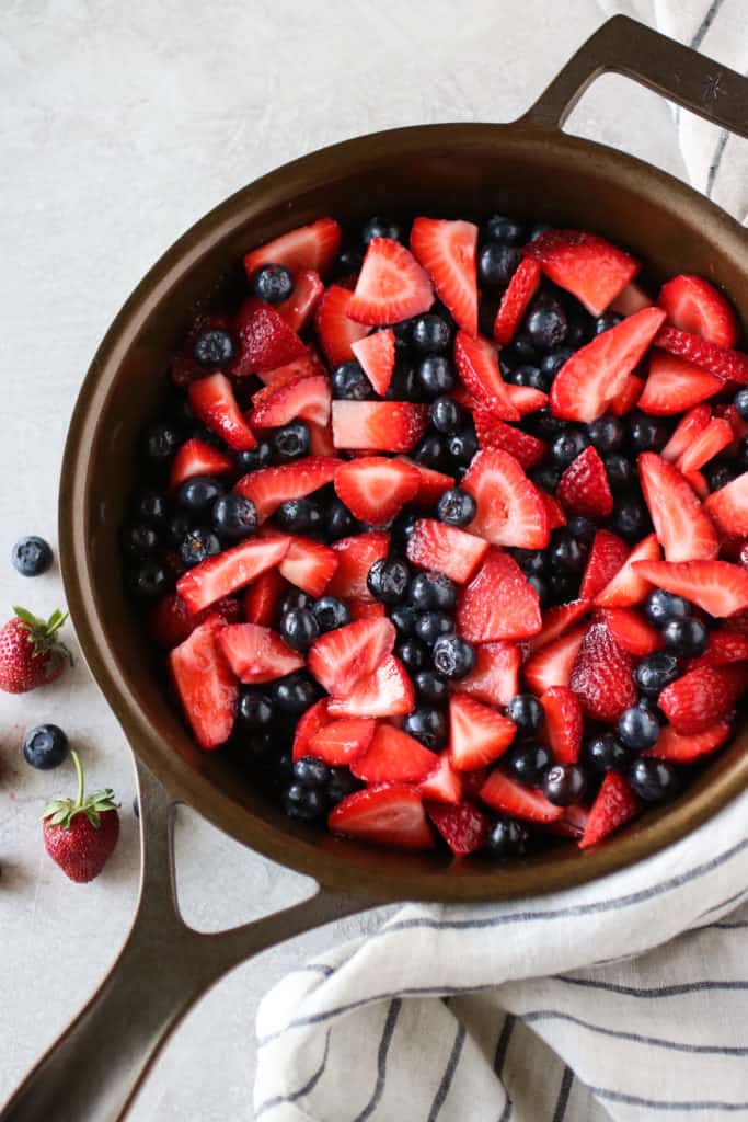 Overhead view of a skillet filled with cut strawberries and blueberries