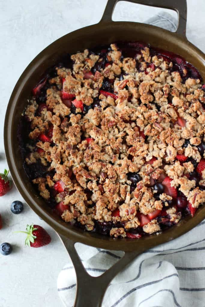 Overhead view of a skillet filled with fresh berries and a grain free crumble on top