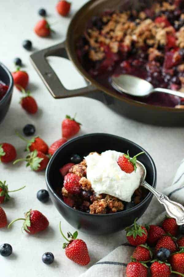Grain-free berry crisp in a bowl with cool whip and strawberry