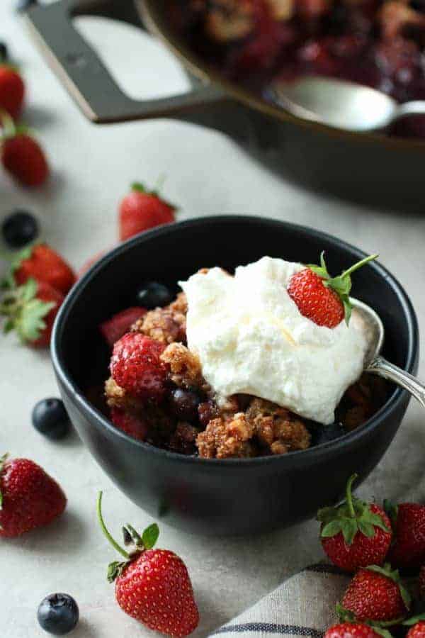 Grain-free berry crisp in a bowl with cool whip and a strawberry