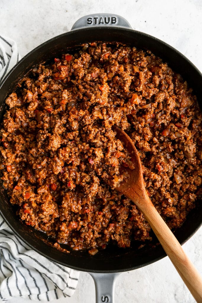 Close up view of a pan of browned ground beef with a wooden spoon in it. 