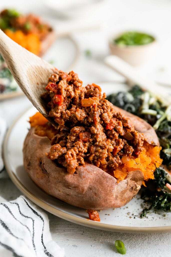 Wooden spoon with sloppy joes mixture filling baked sweet potato