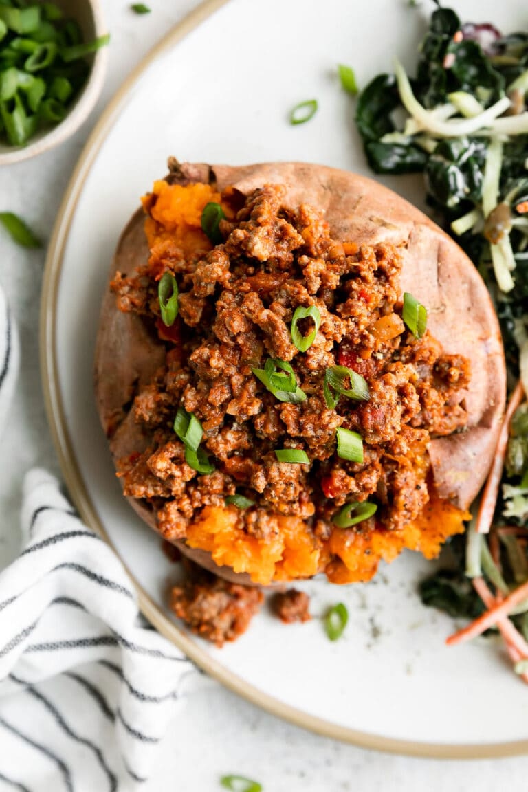 White plate filled with an open sweet potato topped with sloppy joe mixture and side salad. 