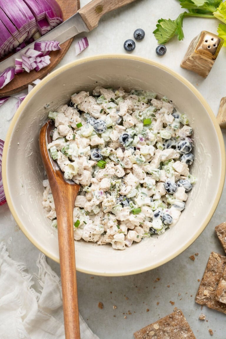 Overhead view of a white bowl filled with fresh blueberry chicken salad with a wooden spoon stuck into the mixture.