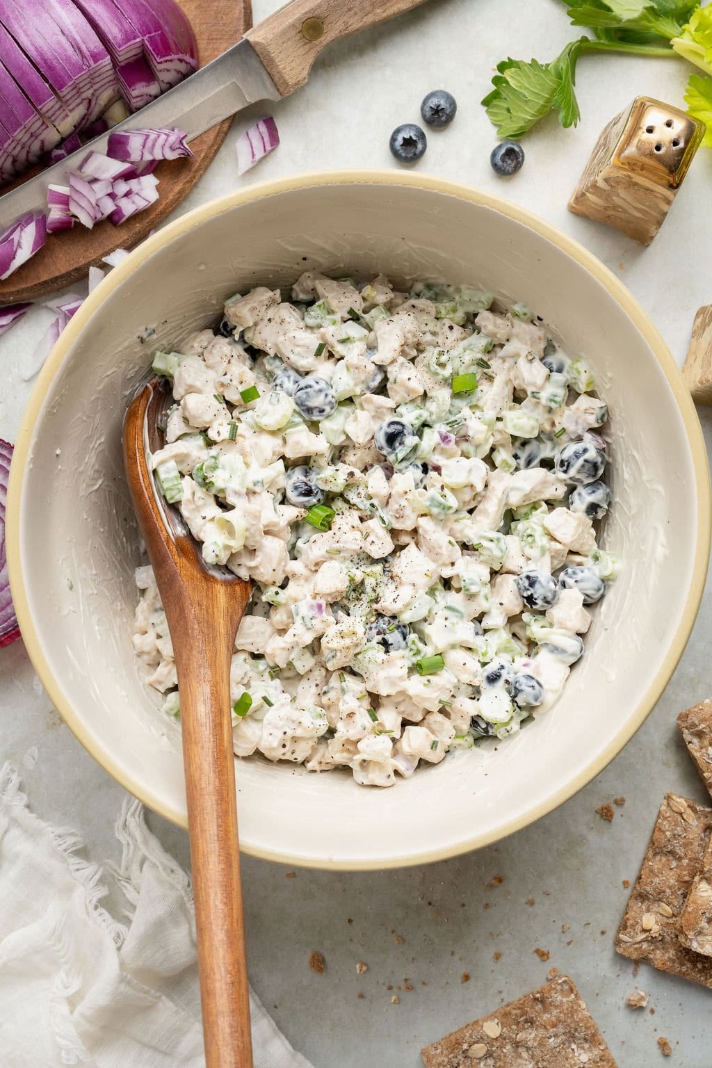 Overhead view of a white bowl of Blueberry Chicken Salad with a wooden spoon stuck into the mixture.