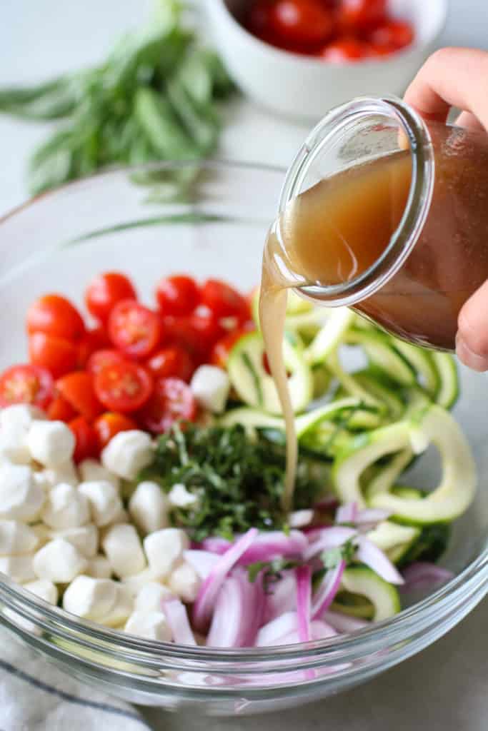 A hand pouring dressing over a Caprese Zucchini Salad 