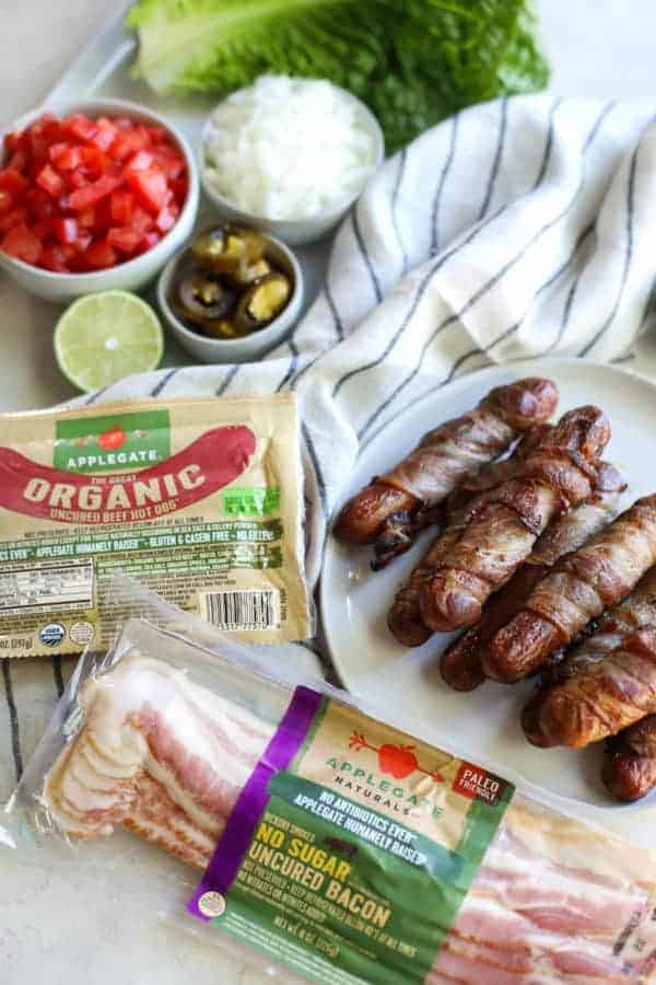 Applegate organic hot dogs and bacon packages beside a plate of bacon wrapped hot dogs