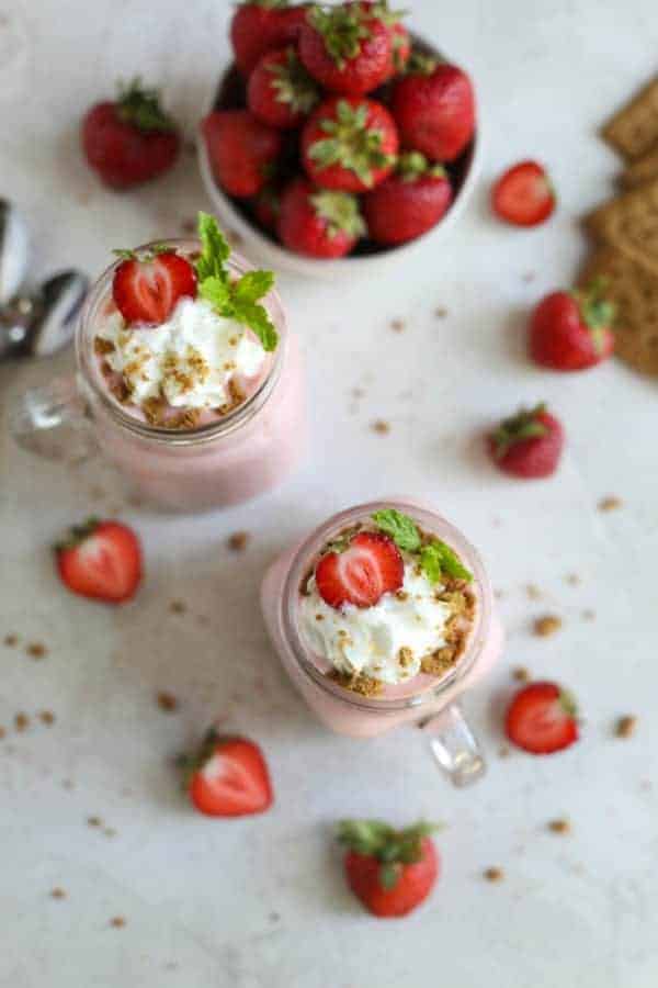 Overhead view of two Strawberry Cheesecake Smoothies with whipped cream and a bowl of fresh strawberries. 