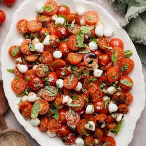 A white serving platter topped with a caprese salad finished with a drizzle of balsamic vinegar.