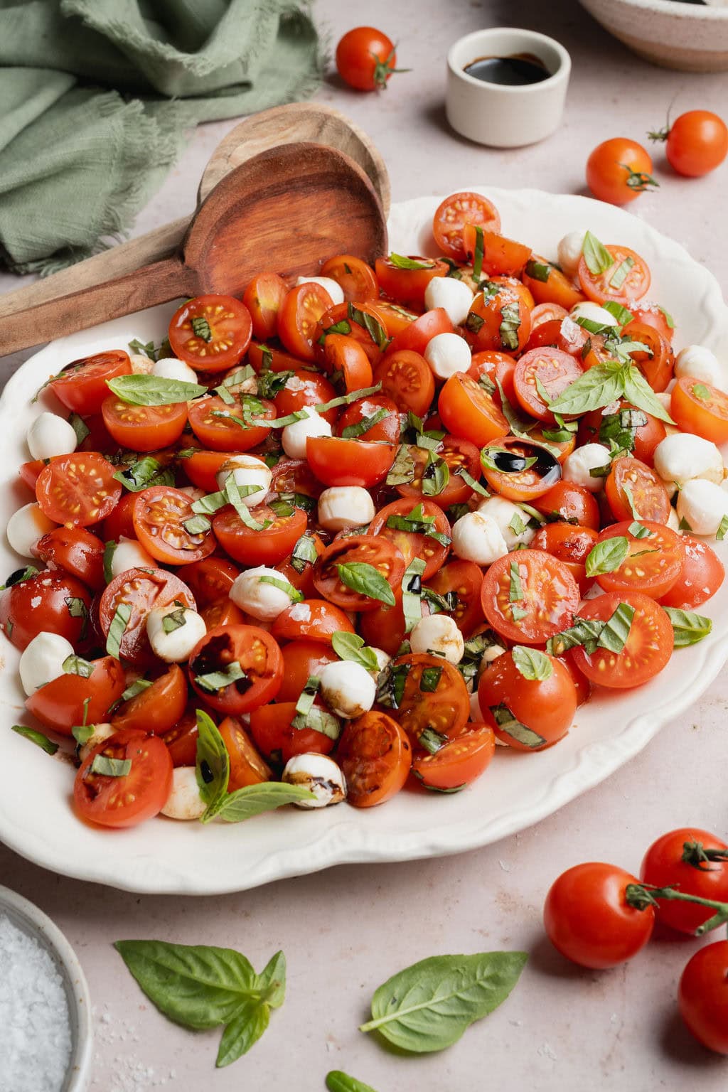 A white platter topped with a caprese salad, two wooden serving spoons on the side.