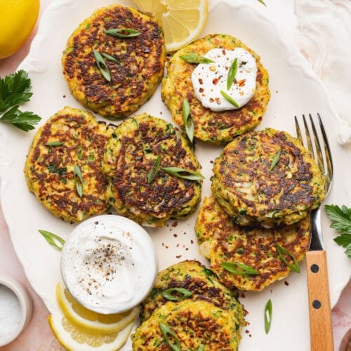 A plate of savory zucchini fritters with a small bowl of white sauce.