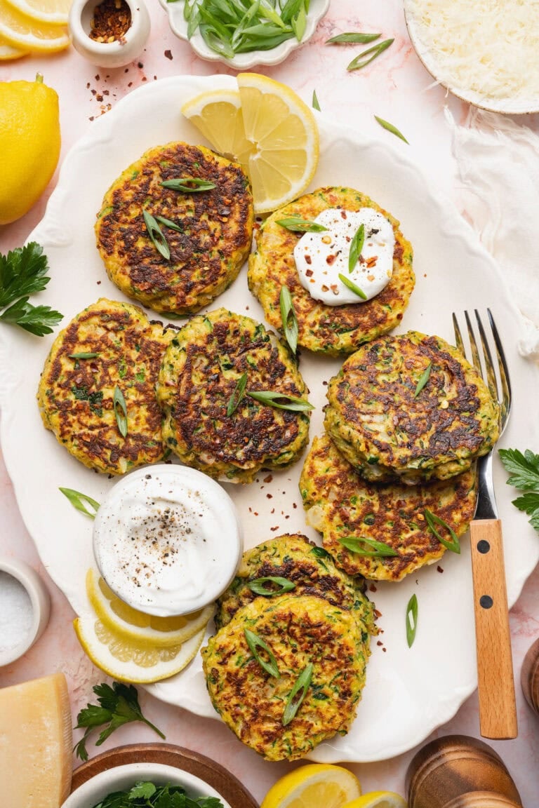 A plate of zucchini fritters with a bowl of mayonnaise and a fork on the side.