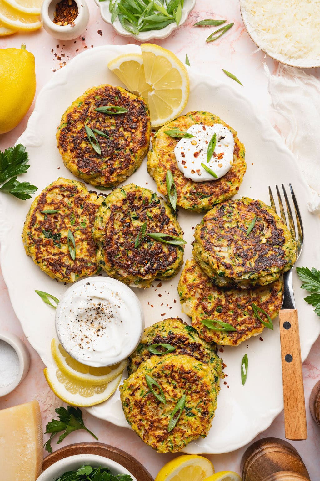 A plate of savory zucchini fritters with a small bowl of white sauce.