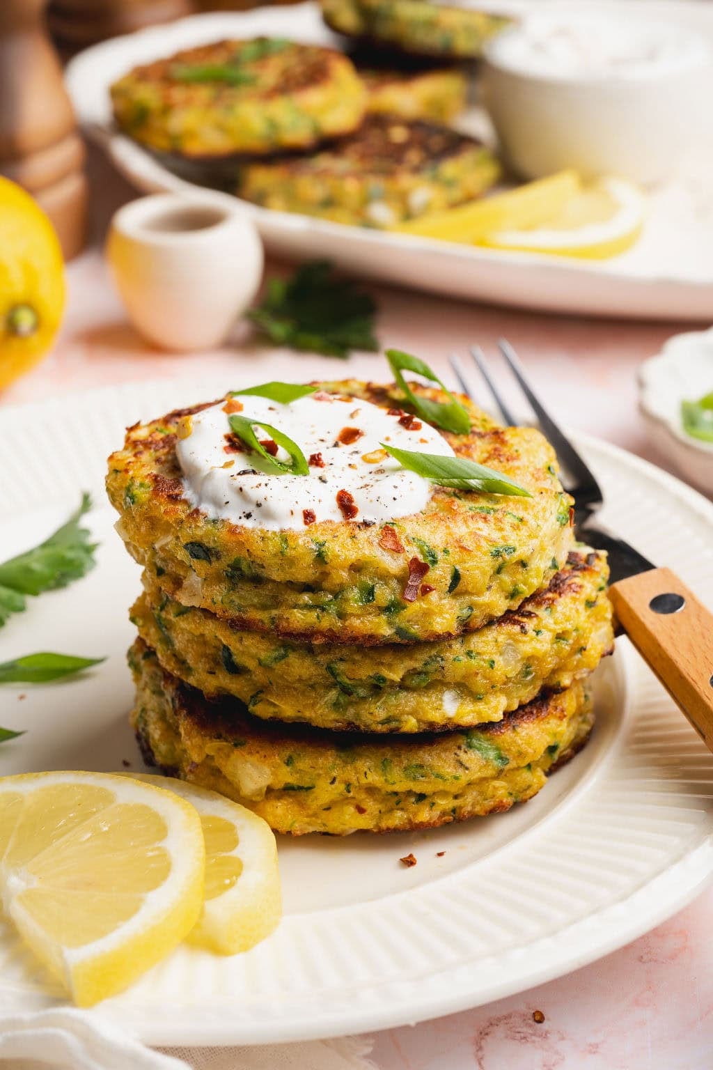A stack of three savory zucchini fritters on a plate, a dollop of mayonnaise on top and a fork on the side.