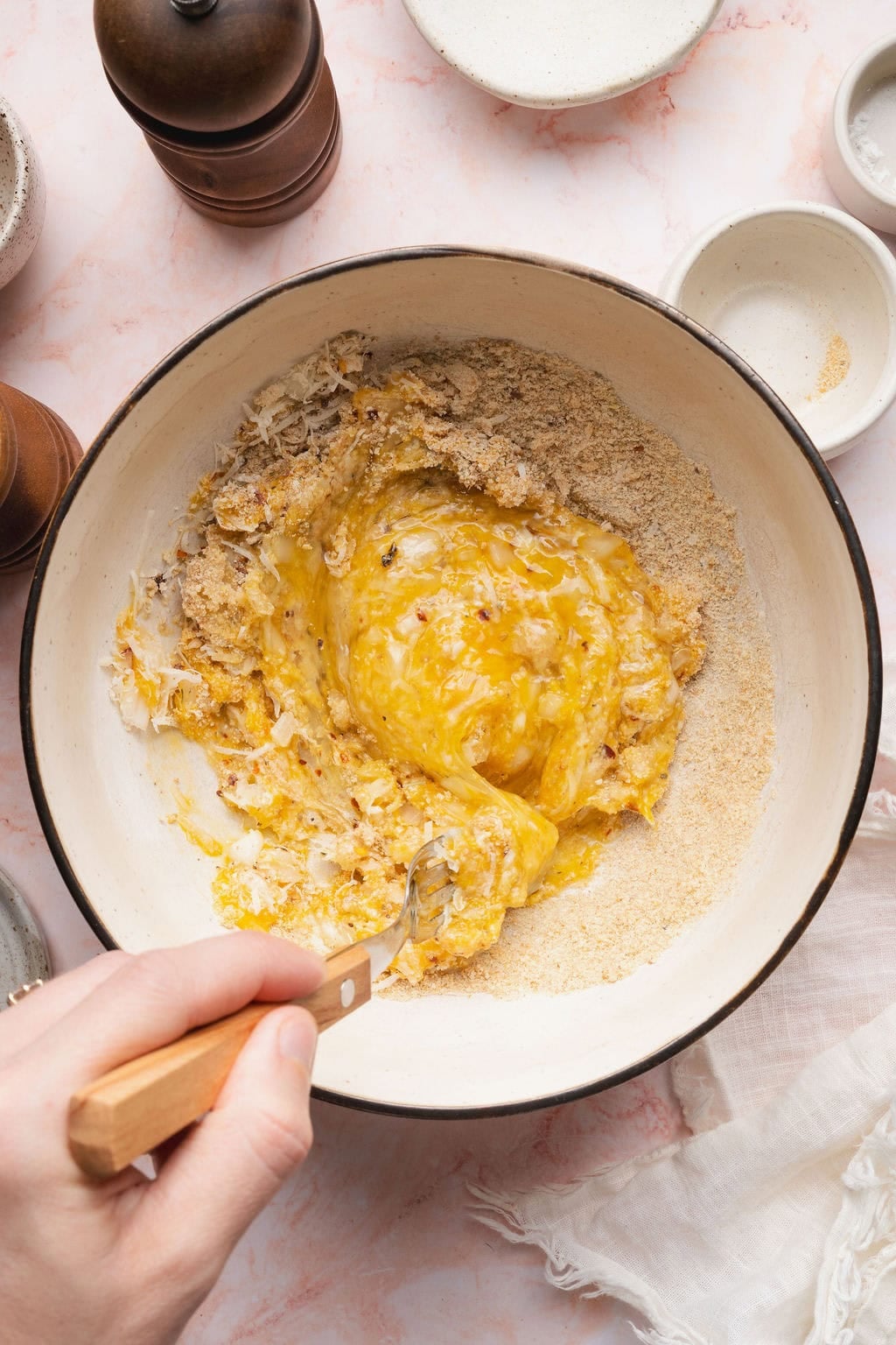 A hand stirring zucchini fritter ingredients with a fork in a bowl.
