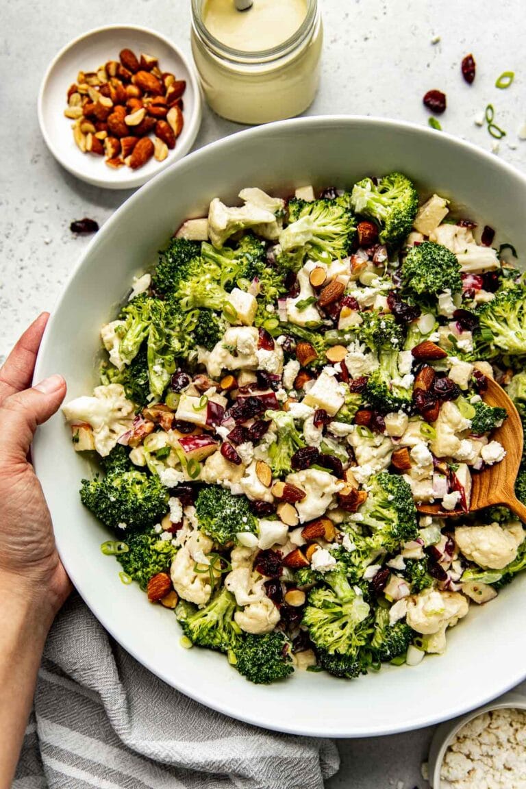 A bowl of apple broccoli cauliflower salad topped with almond pieces and feta crumbles. 