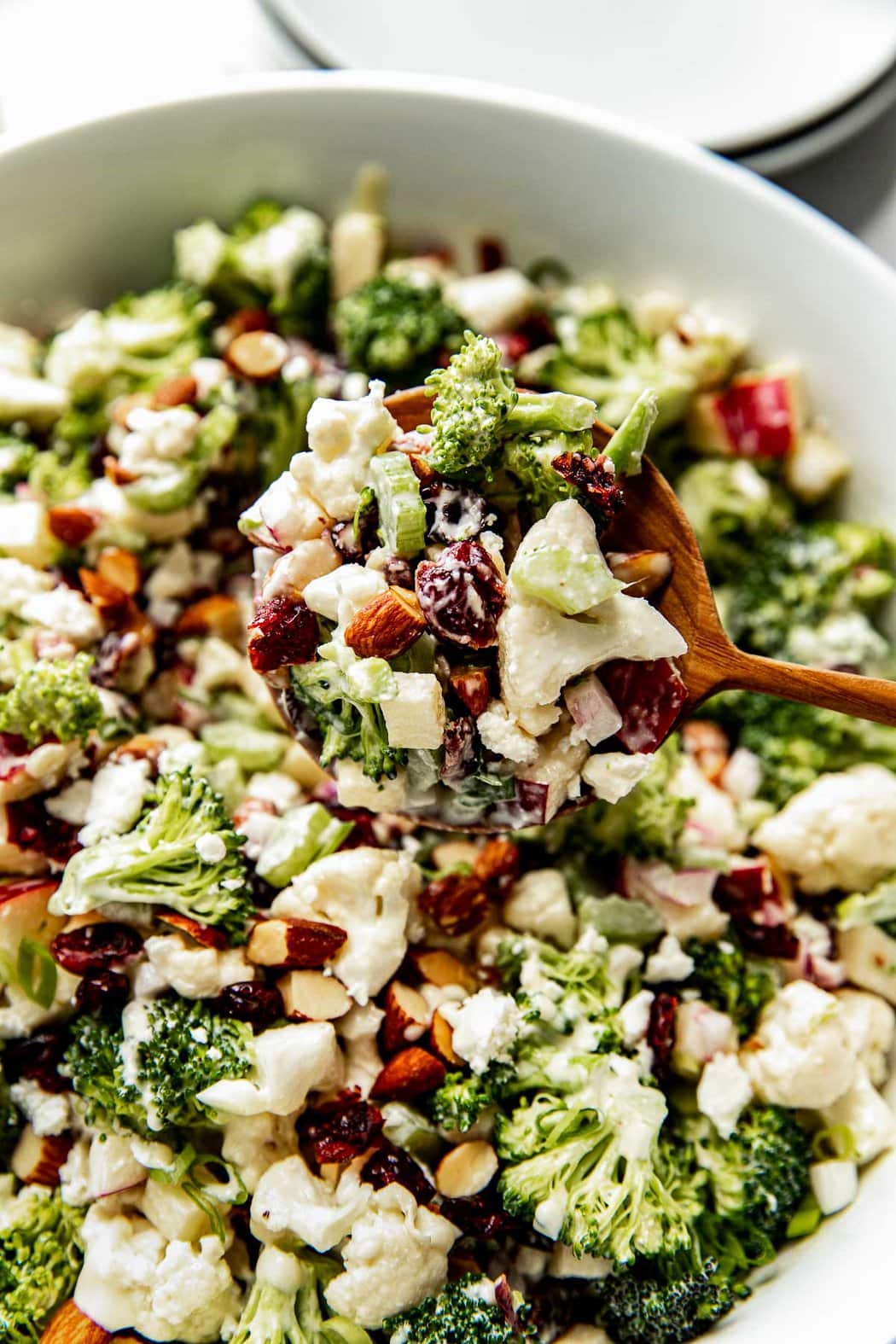 Close up view of a wooden spoon scooping a large portion of freshly combined apple broccoli cauliflower salad. 
