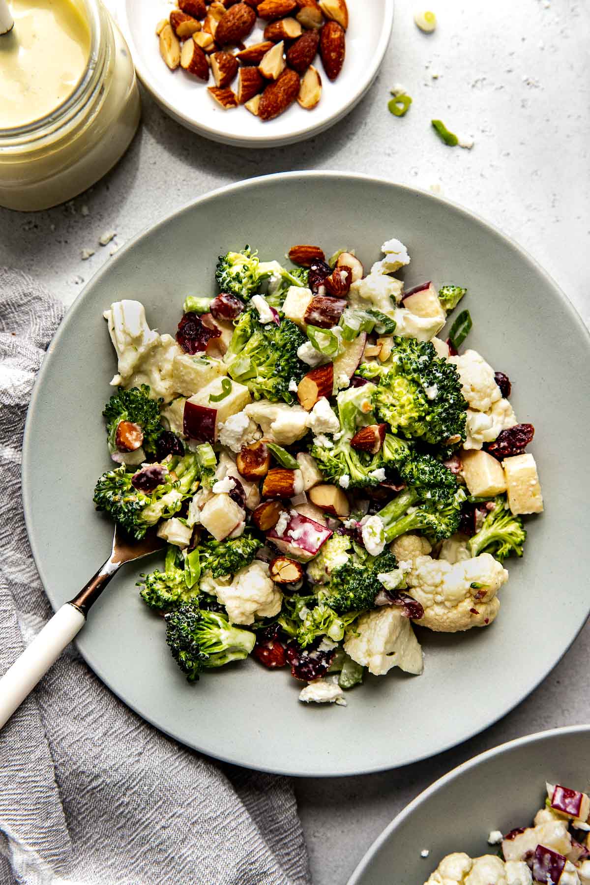 Overhead view of a bowl of apple broccoli cauliflower salad with lemon topped with green onions. 