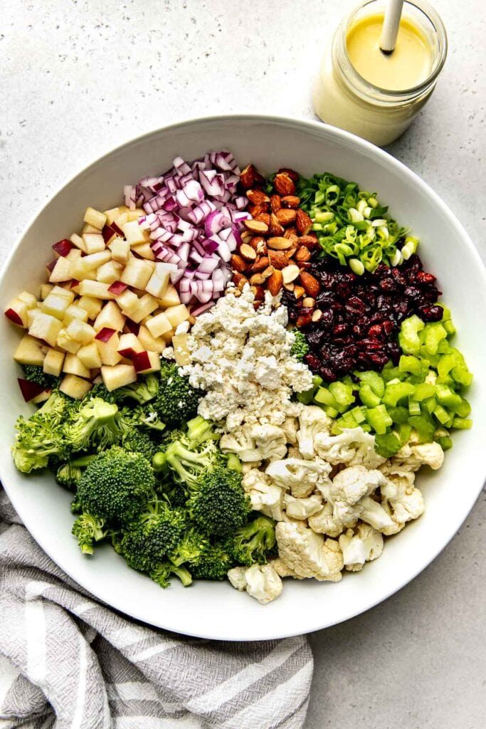 Overhead view of a large bowl with chopped fresh ingredients for apple broccoli cauliflower salad.