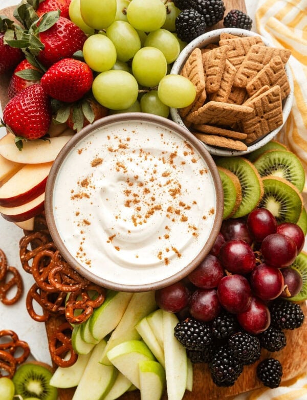 Overhead view of a platter of fresh fruit with a bowl of creamy fruit dip in the middle sprinkled with cinnamon.